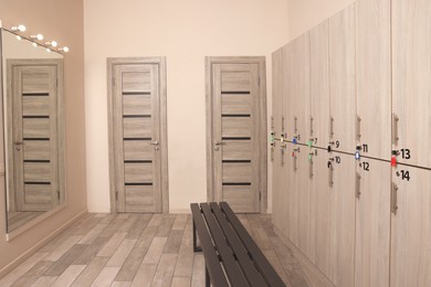 Photo of Wooden bench, mirror and lockers in changing room interior
