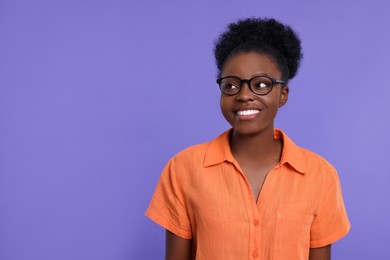 Portrait of happy young woman in eyeglasses on purple background. Space for text