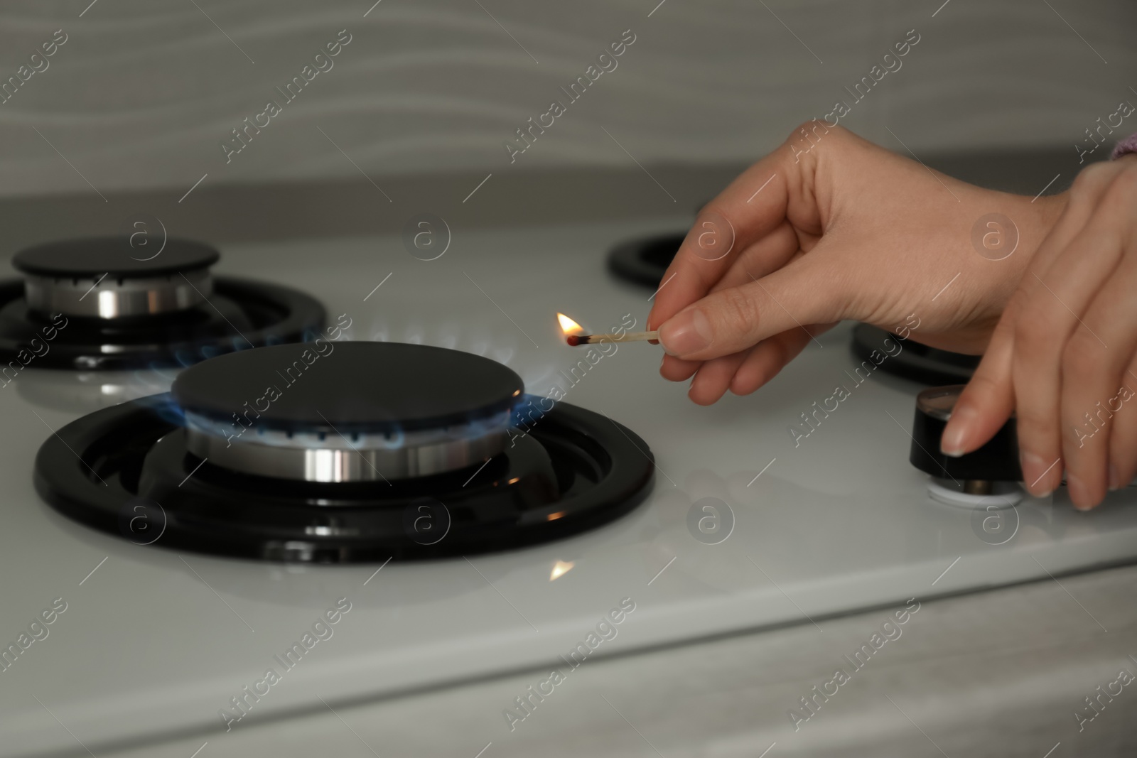 Photo of Woman lighting gas stove with match, closeup