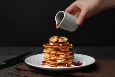 Photo of Woman pouring maple syrup on tasty pancakes