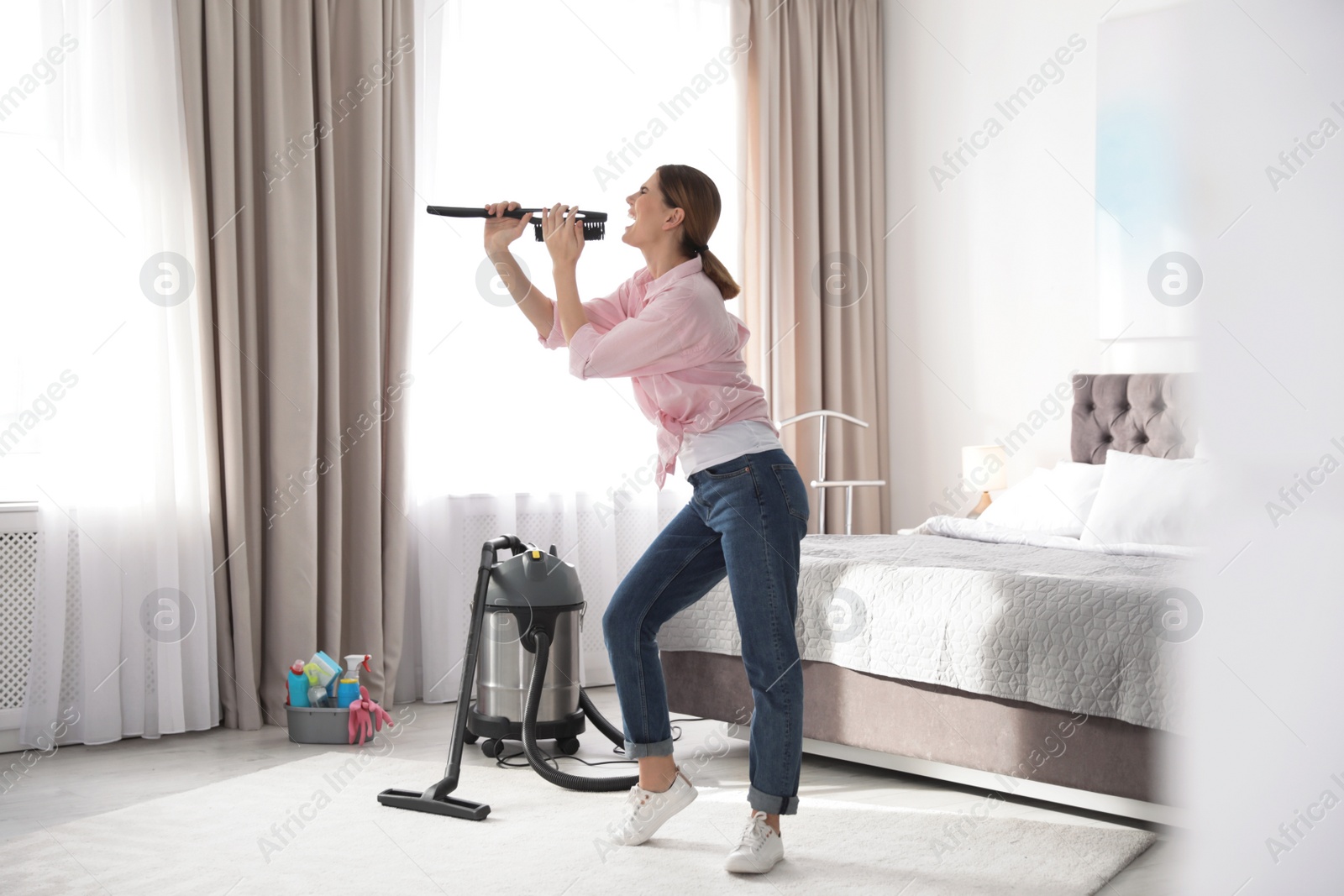 Photo of Happy woman having fun while cleaning bedroom