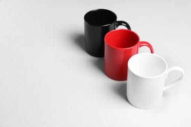 Photo of Colorful ceramic mugs on light background, space for text