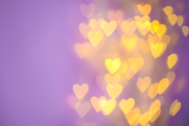 Blurred view of beautiful gold heart shaped lights on violet background