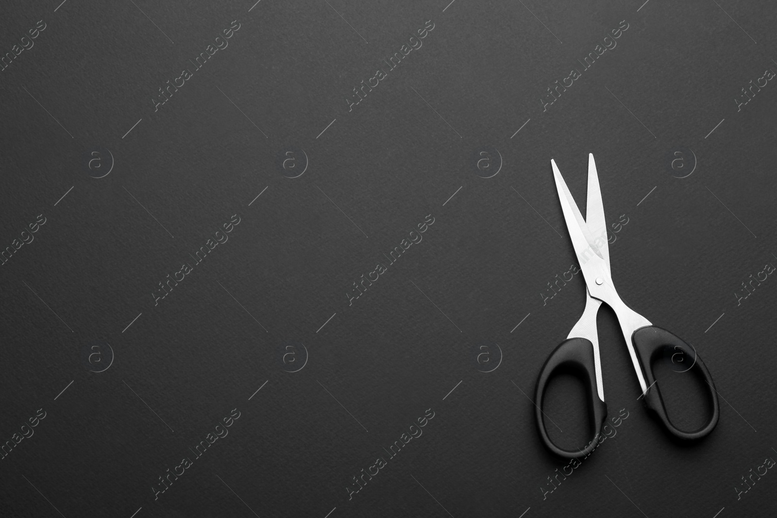 Photo of Pair of sharp scissors on dark background, top view. Space for text