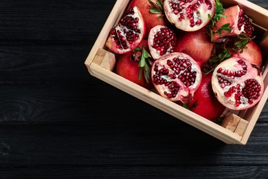 Photo of Delicious ripe pomegranates on black wooden table, top view. Space for text