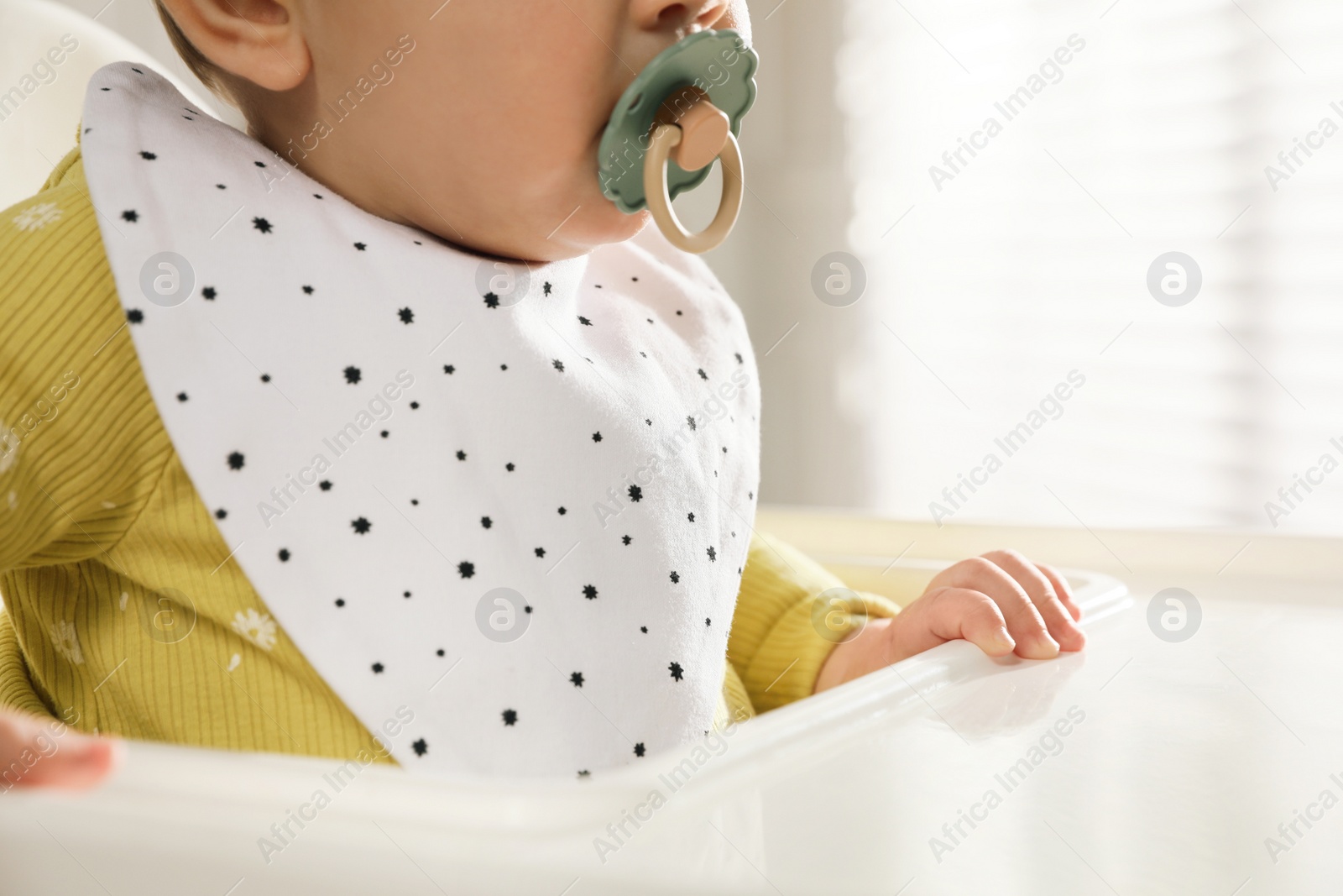 Photo of Cute little baby wearing bib in highchair indoors, closeup