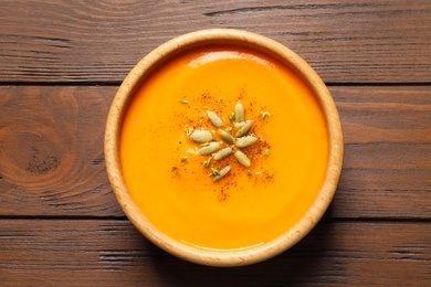 Photo of Bowl with tasty pumpkin soup on wooden table, top view