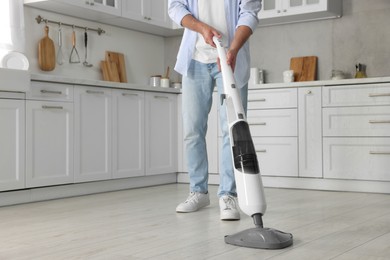 Photo of Man cleaning floor with steam mop in kitchen at home, closeup