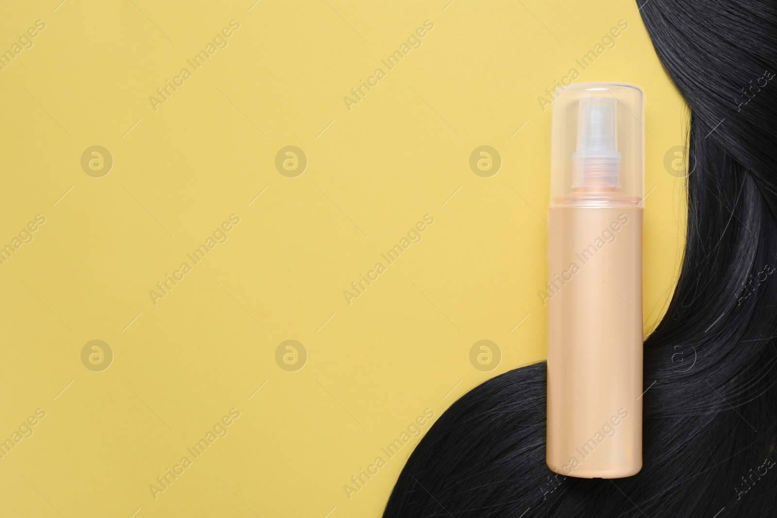 Photo of Spray bottle with thermal protection and lock of black hair on yellow background, flat lay. Space for text
