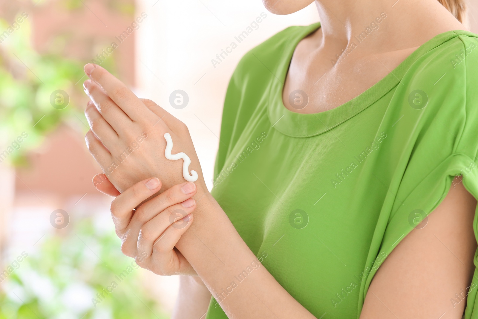 Photo of Young woman applying cream on her hands indoors, closeup