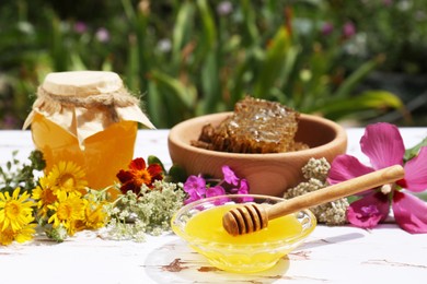 Photo of Delicious honey, combs and different flowers on white wooden table in garden