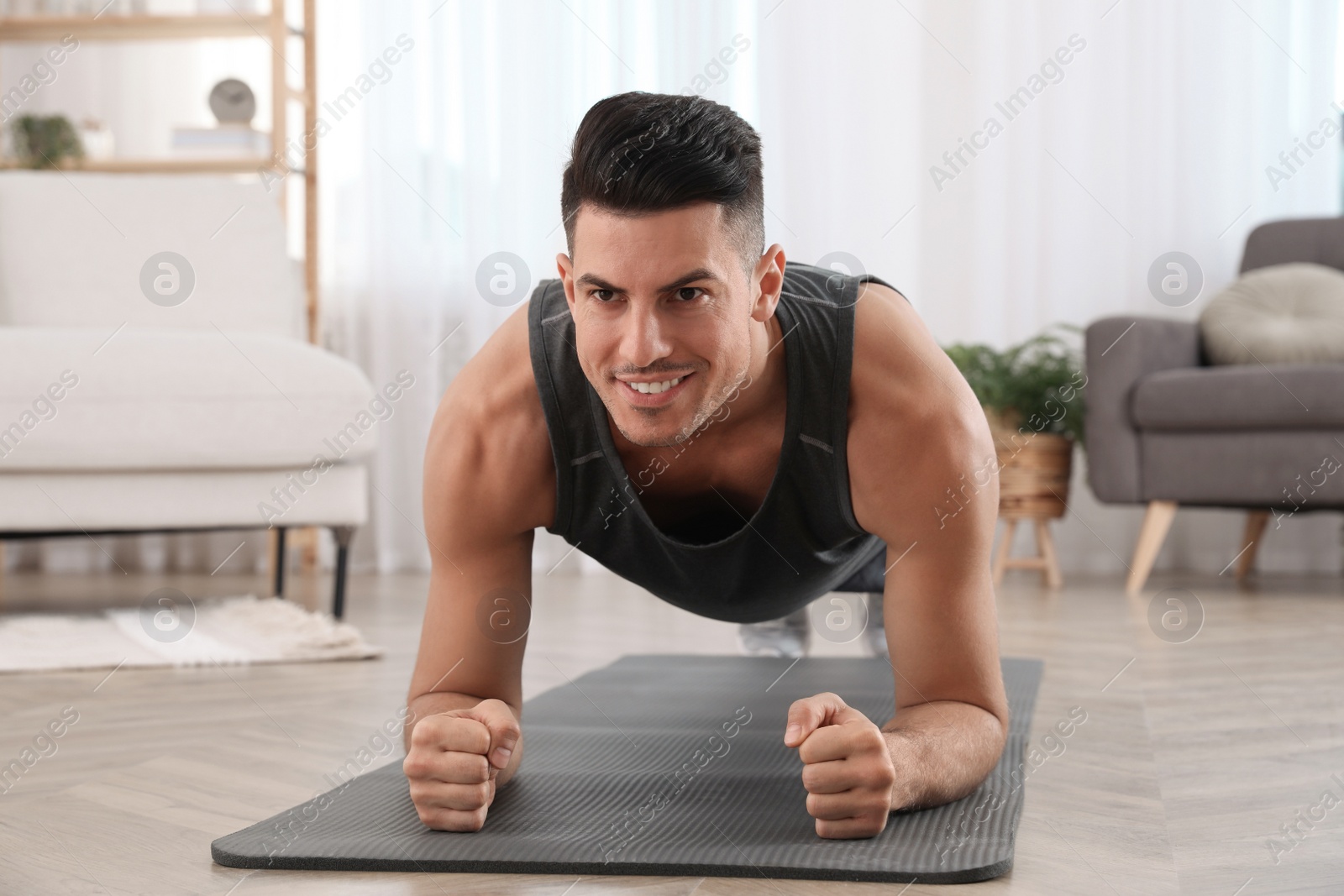 Photo of Handsome man doing plank exercise on yoga mat at home