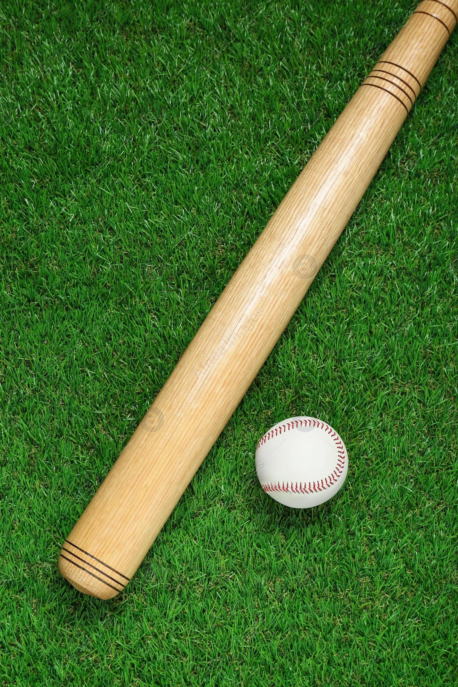 Photo of Wooden baseball bat and ball on green grass, flat lay. Sports equipment