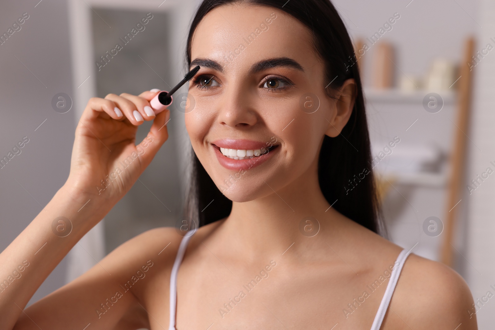 Photo of Beautiful young woman applying mascara indoors, closeup