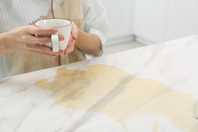 Photo of Woman with spilled coffee over her shirt at marble table indoors, closeup