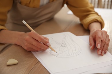 Photo of Young woman drawing female portrait at table indoors, closeup