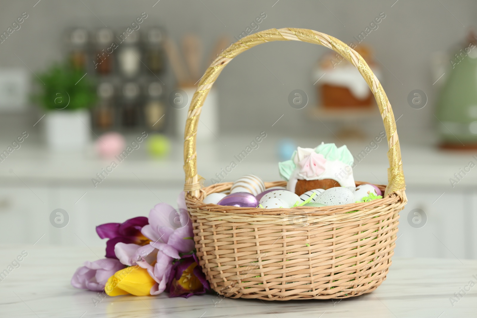 Photo of Wicker basket with painted eggs and delicious Easter cake near tulips on white marble table indoors