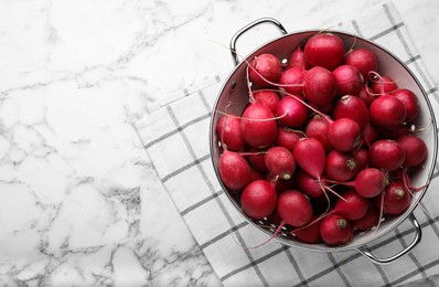 Photo of Colander with fresh ripe radishes on white marble table, top view. Space for text