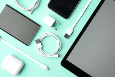 Photo of USB charge cables, power adapter and gadgets on light blue background, flat lay. Modern technology