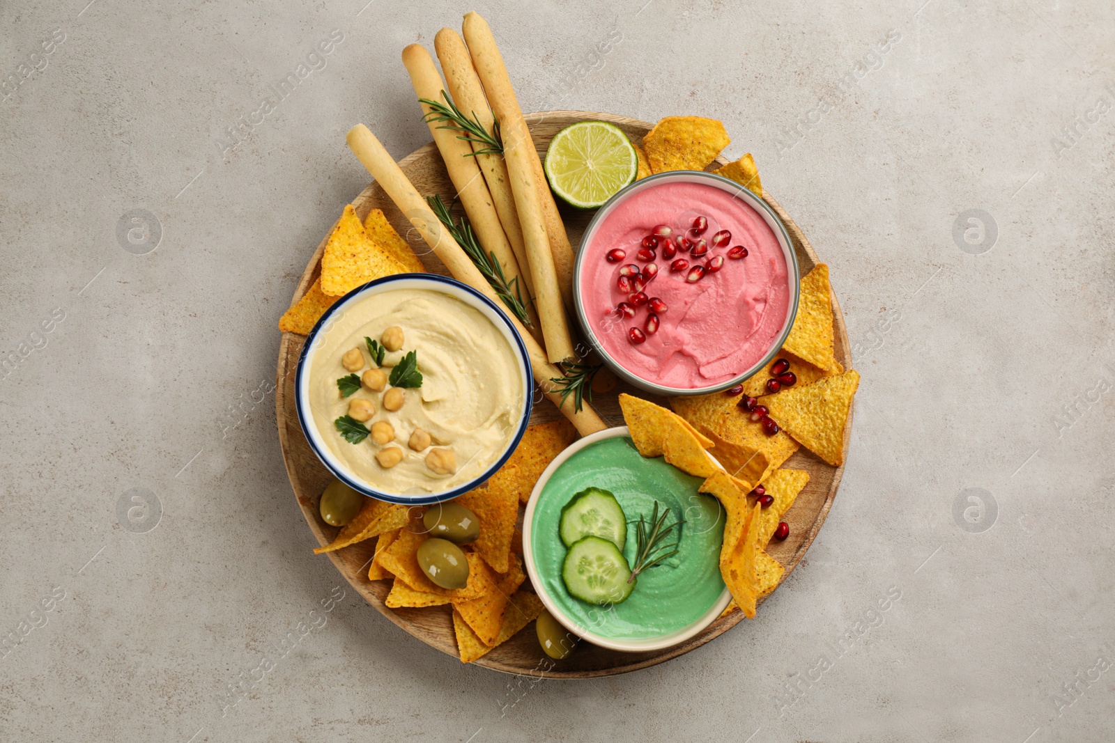 Photo of Different kinds of tasty hummus served with snacks on light table, top view