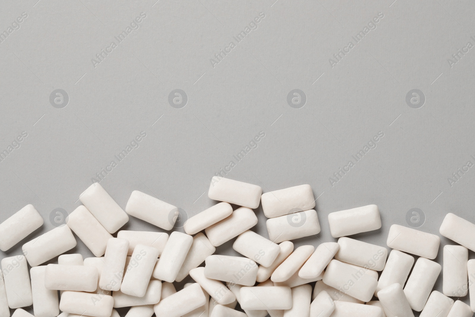 Photo of Many chewing gum pieces on light grey background, flat lay. Space for text