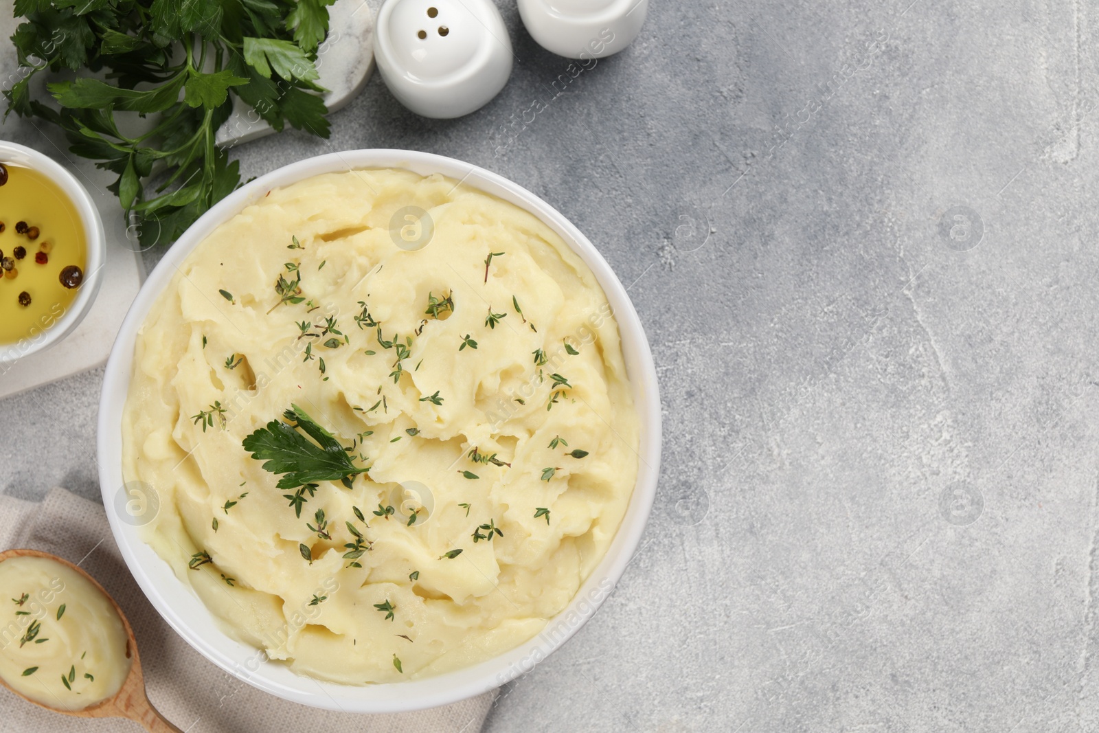 Photo of Bowl of tasty mashed potato, parsley, olive oil and pepper on grey marble table, flat lay. Space for text