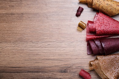 Delicious fruit leather rolls on wooden table, flat lay. Space for text