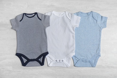 Photo of Different baby bodysuits on wooden background, top view