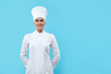 Photo of Happy female chef wearing uniform and cap on light blue background. Space for text