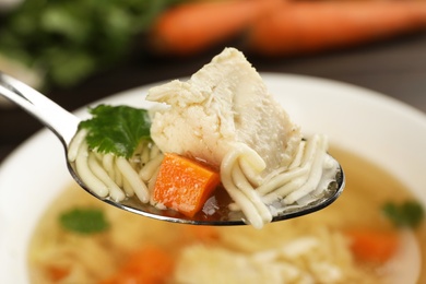 Photo of Spoon with fresh homemade chicken soup on blurred background, closeup