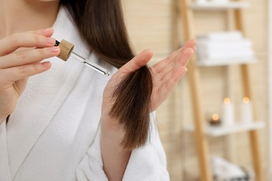 Photo of Woman applying essential oil onto hair in bathroom, closeup and space for text