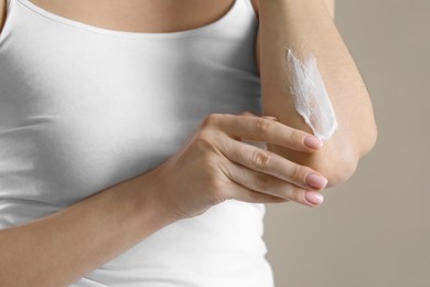 Photo of Woman applying body cream onto elbow on beige background, closeup