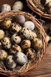 Photo of Wicker bowl with quail eggs and straw on wooden table, flat lay