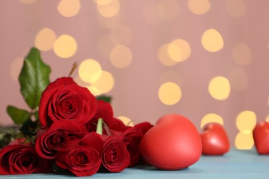 Photo of Beautiful red roses and decorative hearts on table against blurred lights, space for text. St. Valentine's day celebration