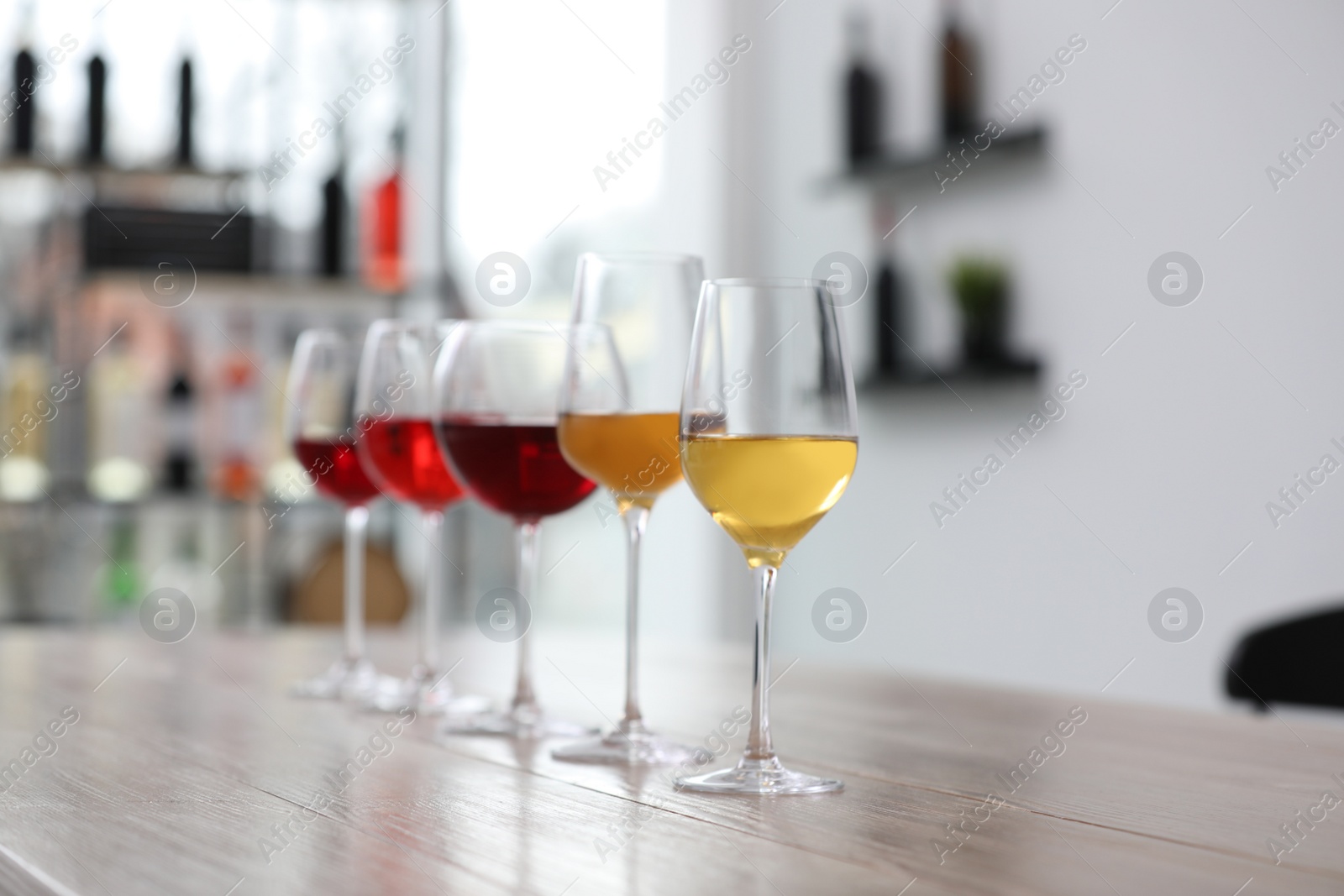 Photo of Different sorts of wine in glasses prepared for tasting on wooden table indoors