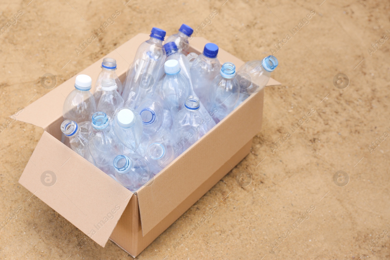 Photo of Cardboard box with used plastic bottles on sand. Recycling problem