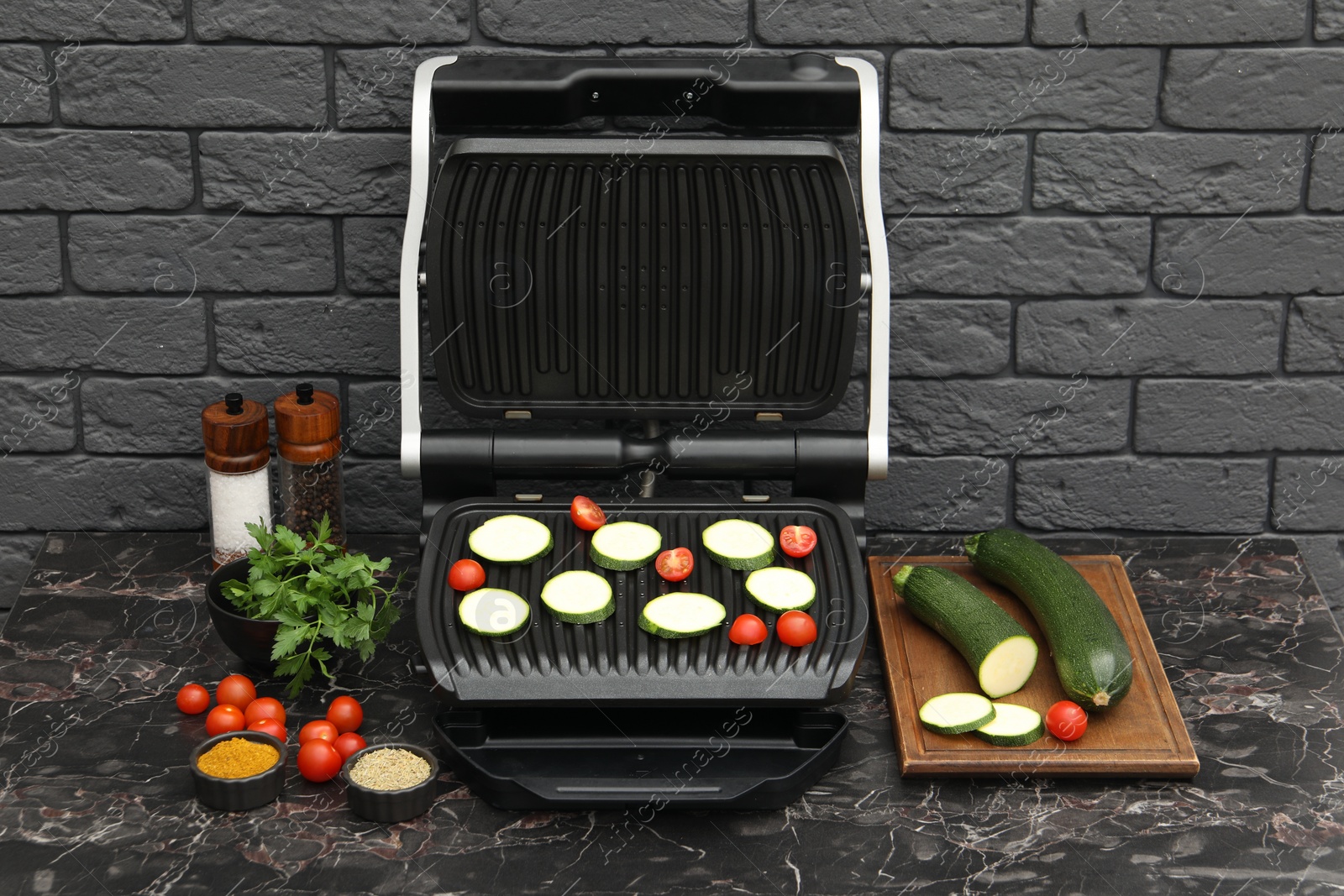 Photo of Electric grill with vegetables and spices on black marble table