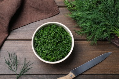 Fresh dill, knife and napkin on wooden table, flat lay