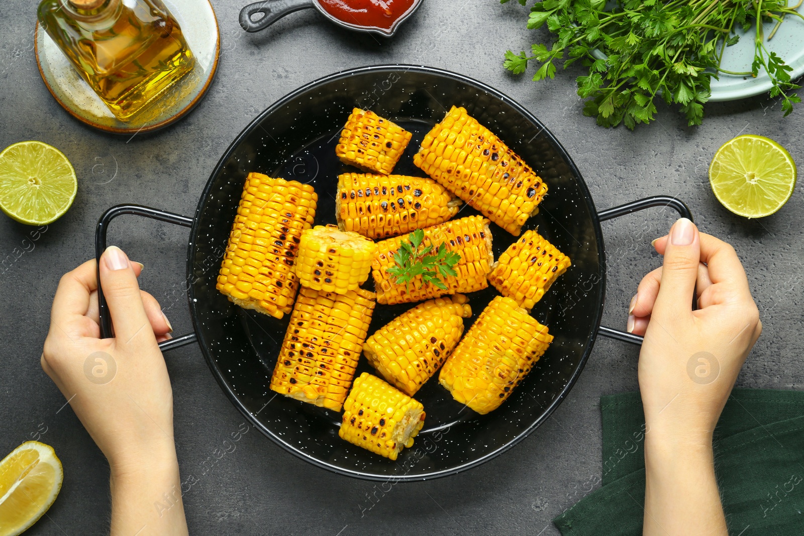 Photo of Woman holding pan with tasty grilled corn at dark grey table, top view