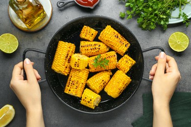 Woman holding pan with tasty grilled corn at dark grey table, top view