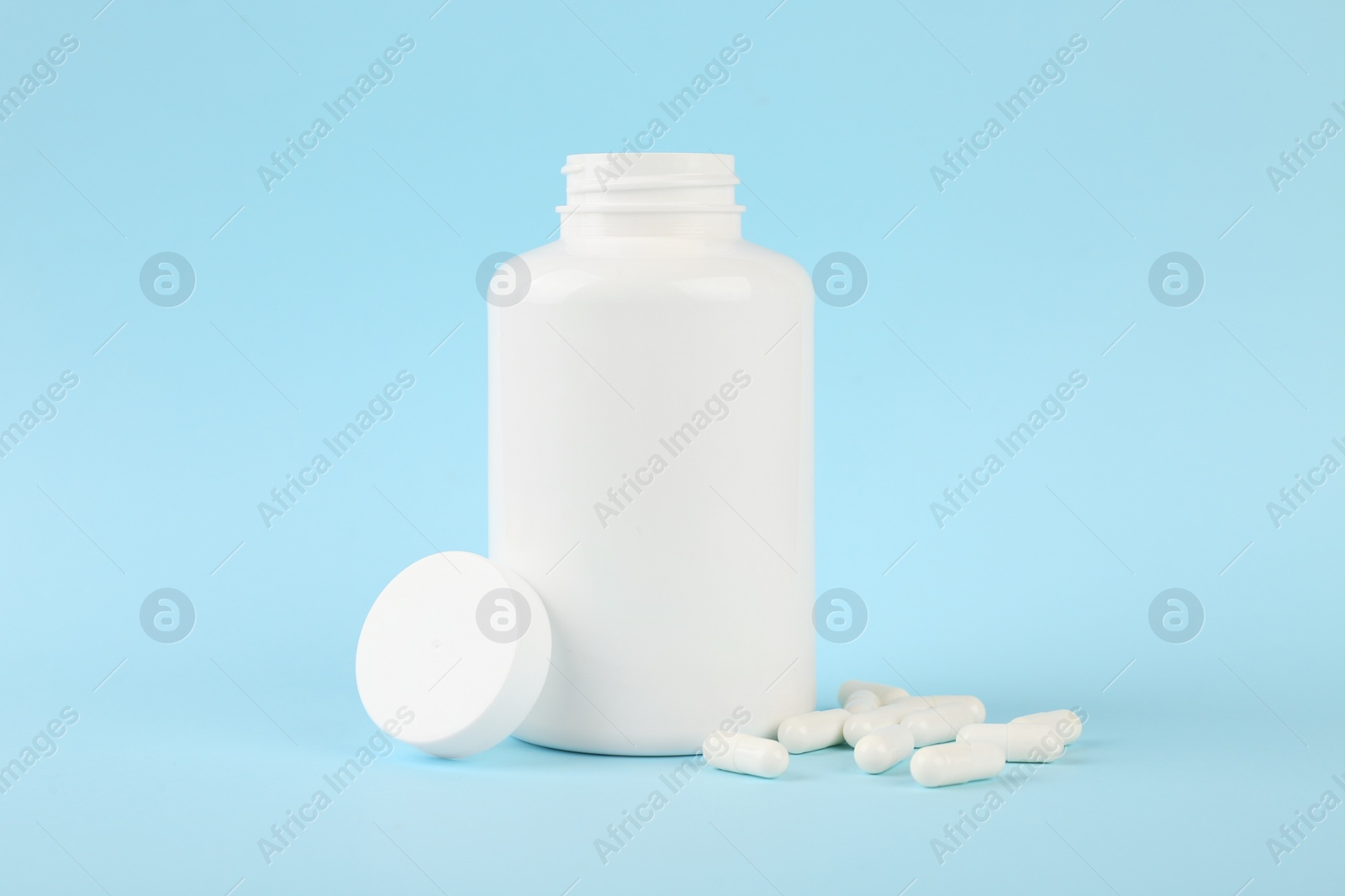 Photo of Blank white jar with vitamin capsules on light blue background, space for text