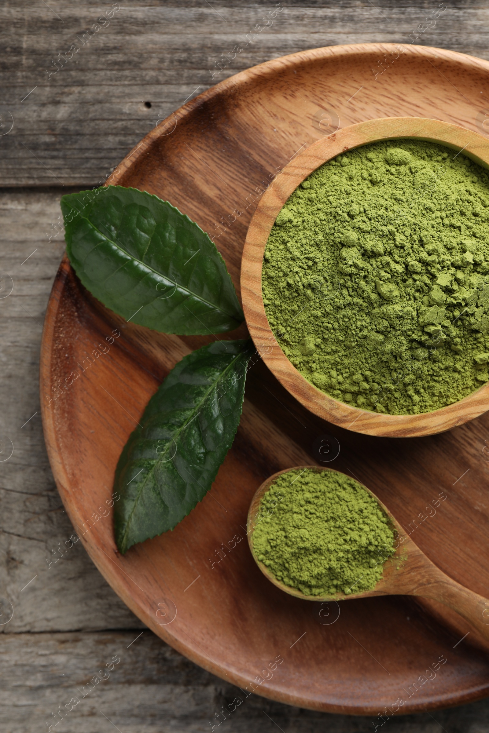 Photo of Green matcha powder and leaves on wooden table, top view