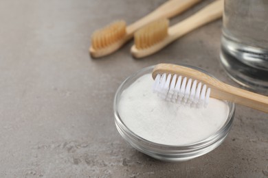 Bamboo toothbrushes and bowl of baking soda on grey table, closeup. Space for text