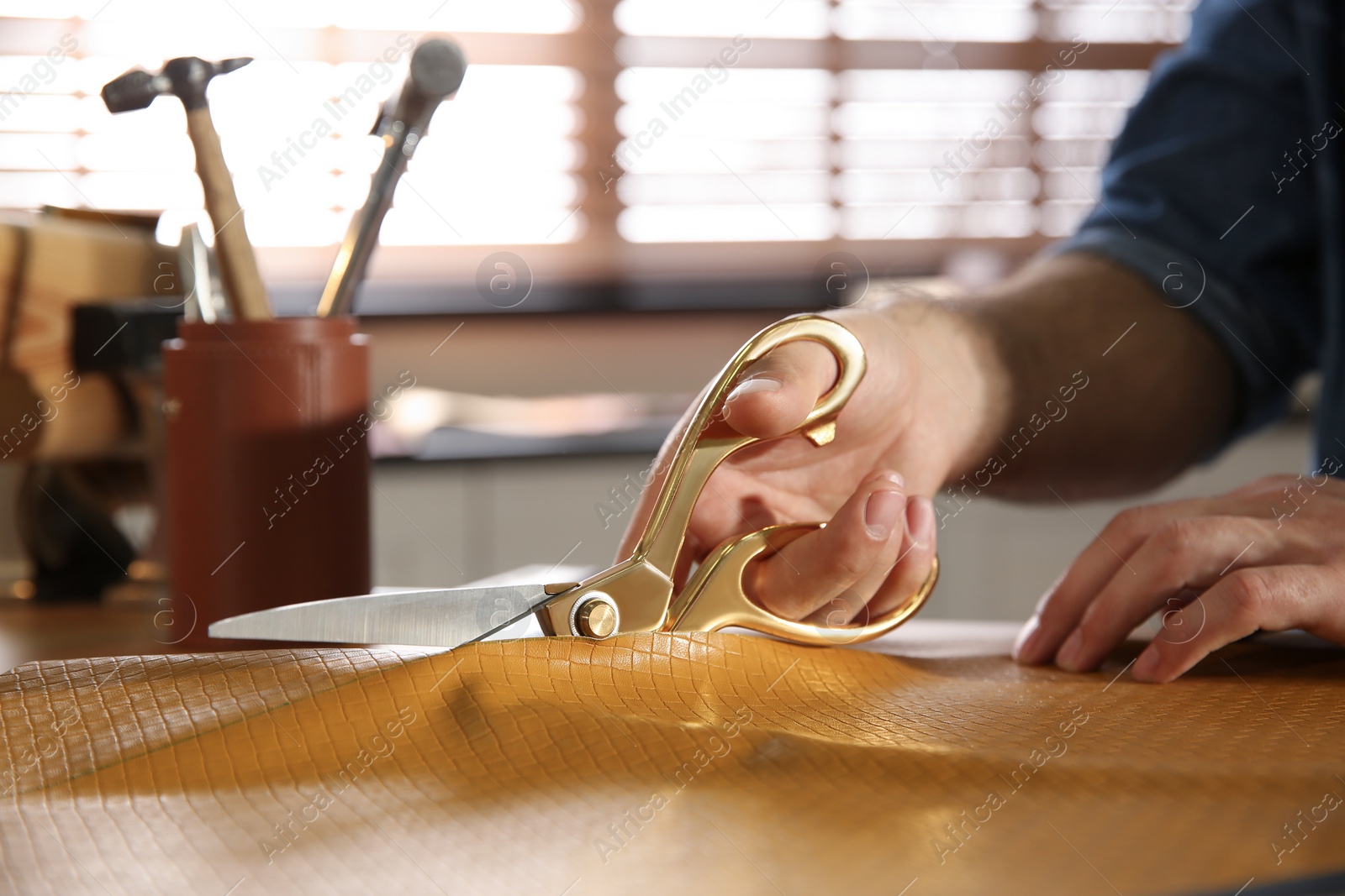 Photo of Man cutting leather with scissors in workshop, closeup