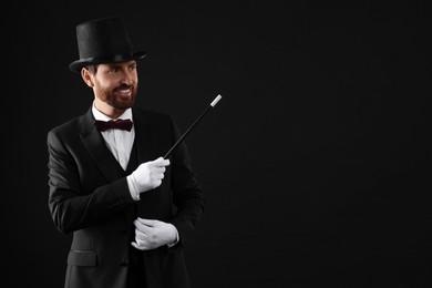 Happy magician holding wand on black background, space for text