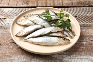 Photo of Fresh raw sprats and parsley on wooden table, closeup