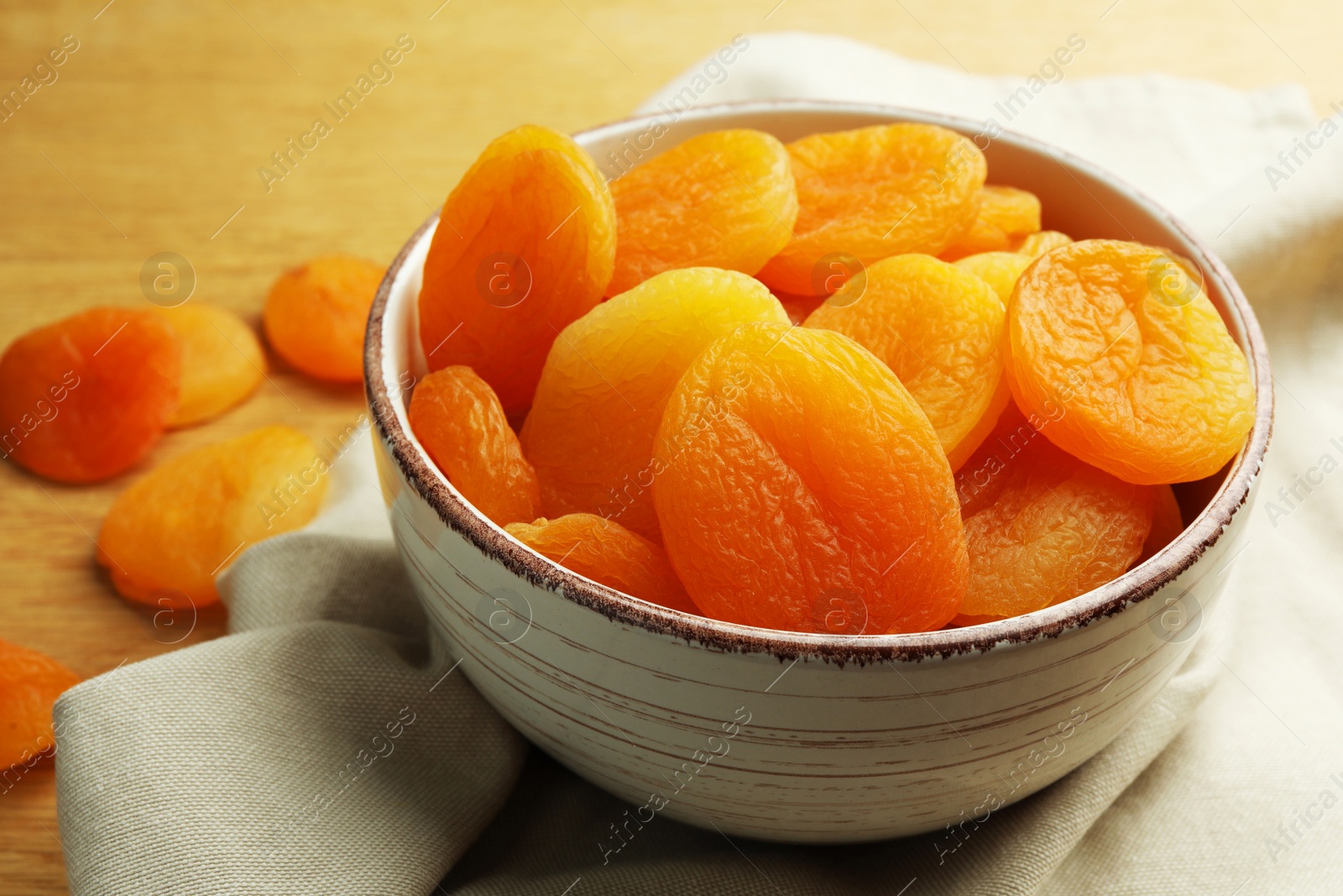 Photo of Bowl of tasty apricots on wooden table, closeup. Dried fruits