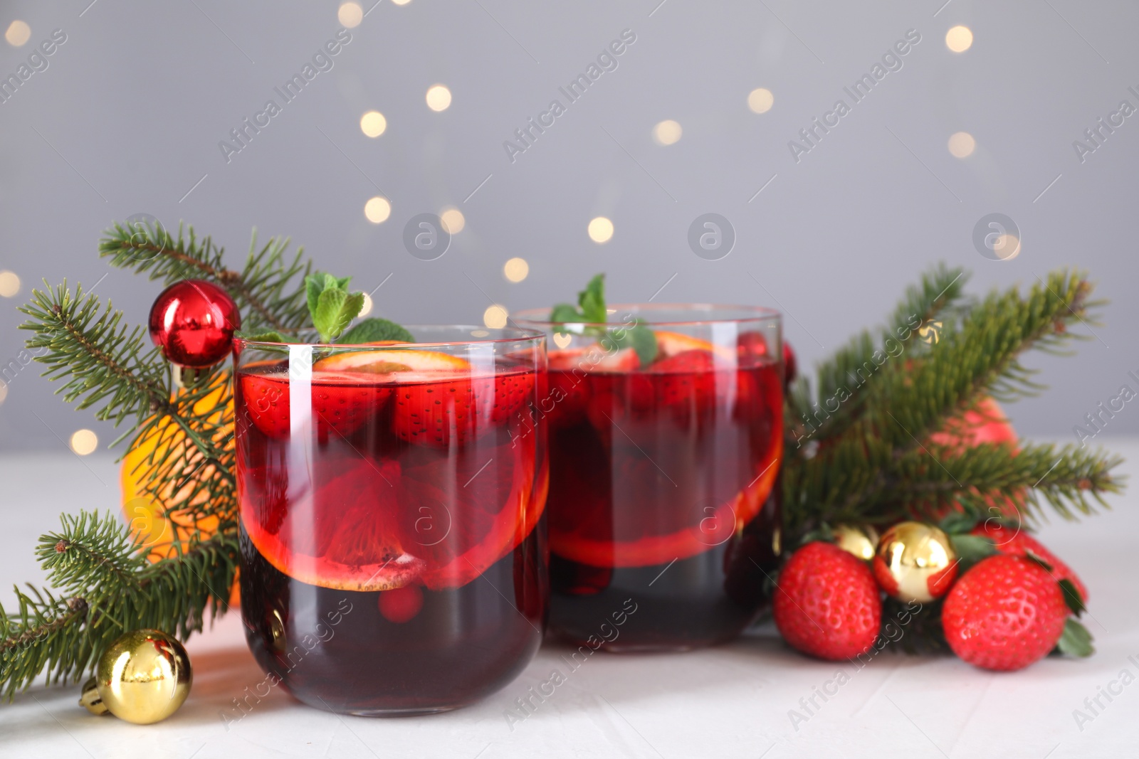 Photo of Aromatic Christmas Sangria in glasses and festive decor on white table, closeup