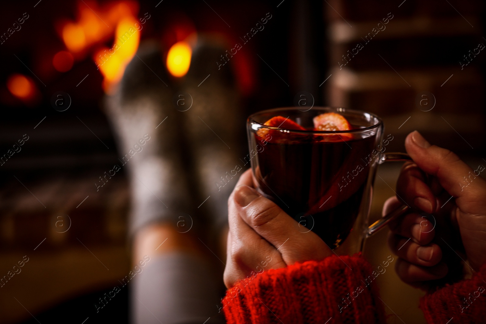 Photo of Woman with tasty mulled wine near burning fireplace indoors, closeup