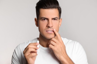 Photo of Man with herpes applying cream on lips against light grey background